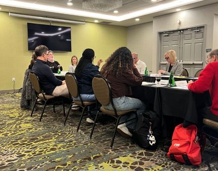 A number of people sitting around a table in a meeting