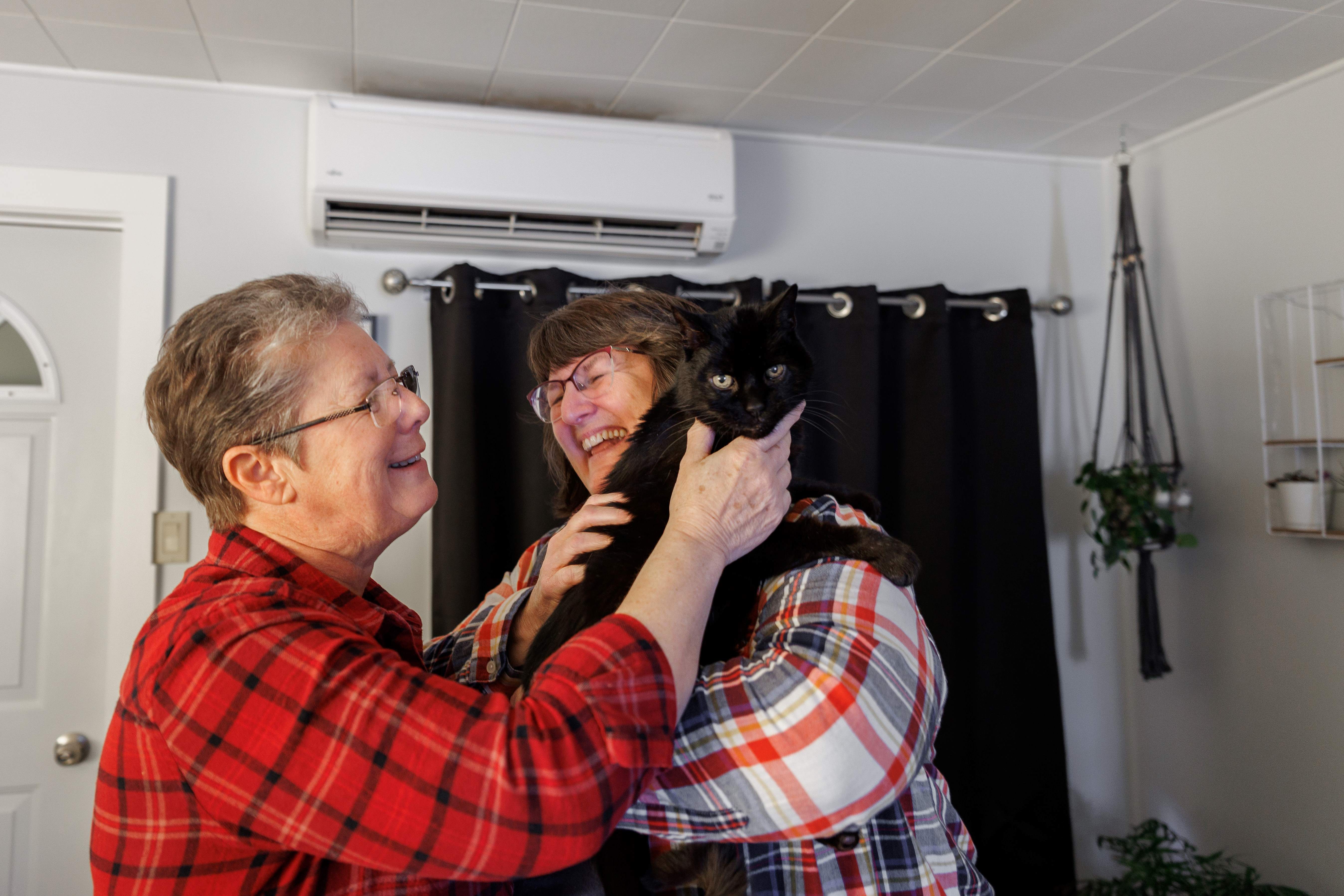 Two women smiling while holding a black cat